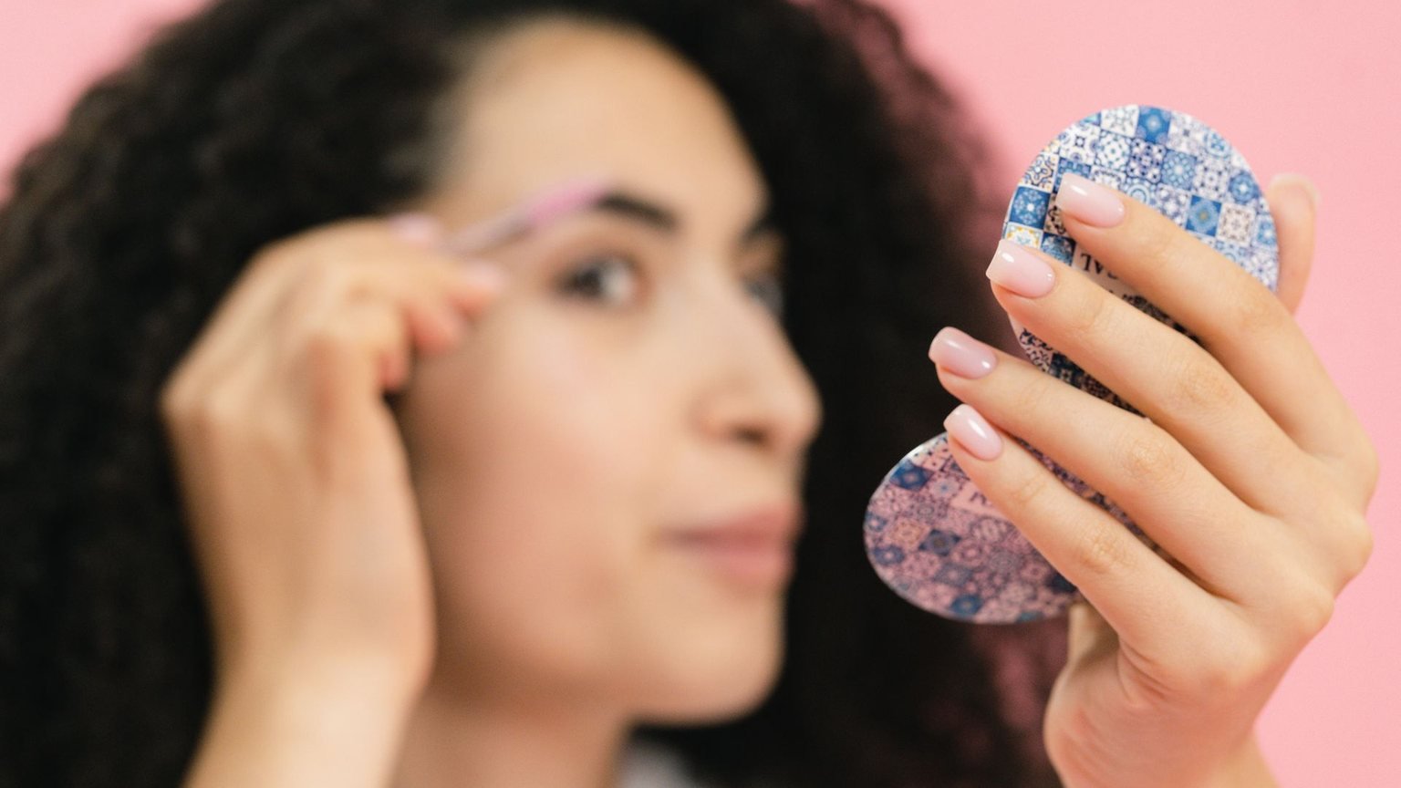 Woman applying the best eyebrow gel for oily skin while checking her brow in a mirror