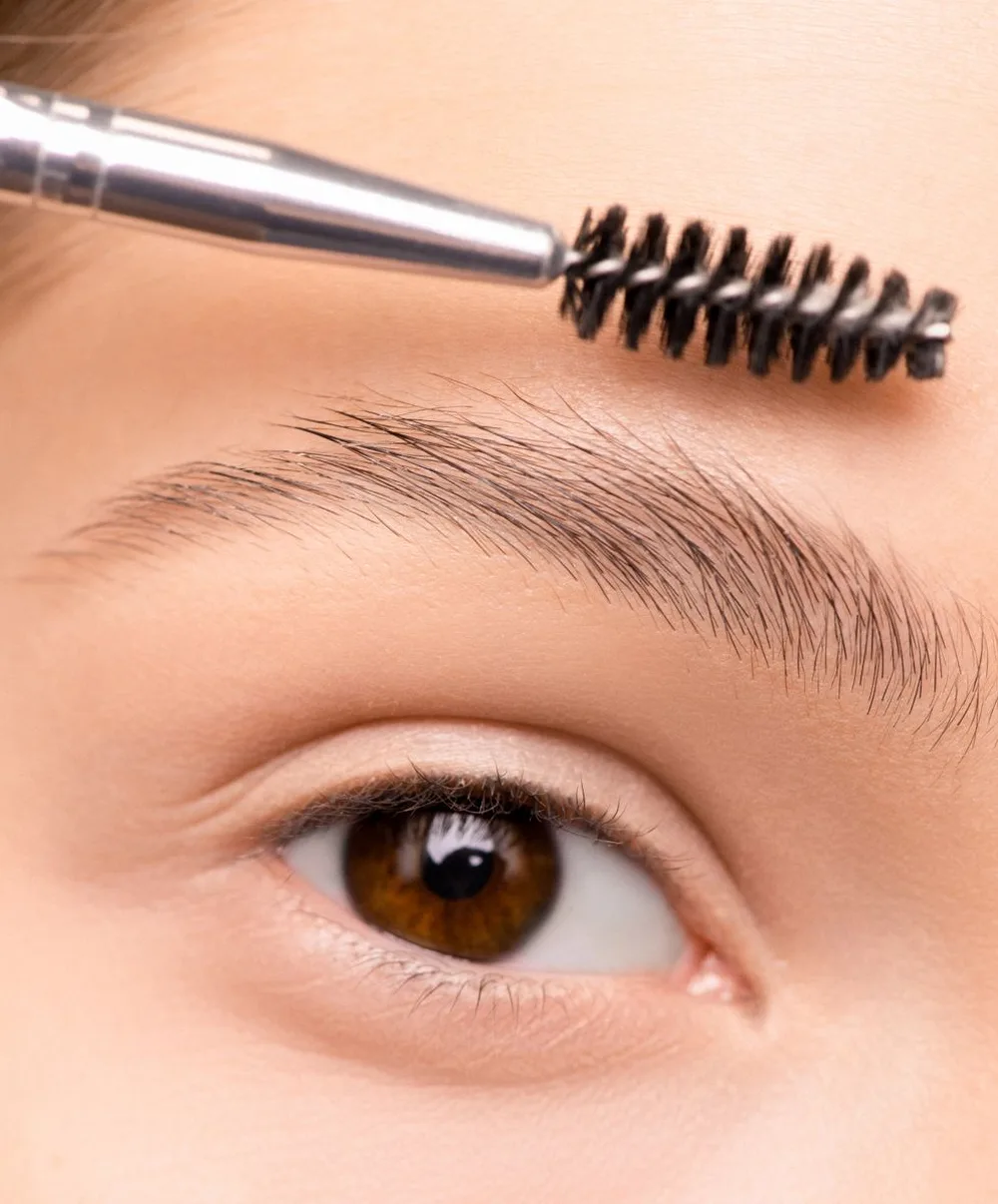 Macro close-up of a spoolie brush applying eyebrow gel to individual brow hairs