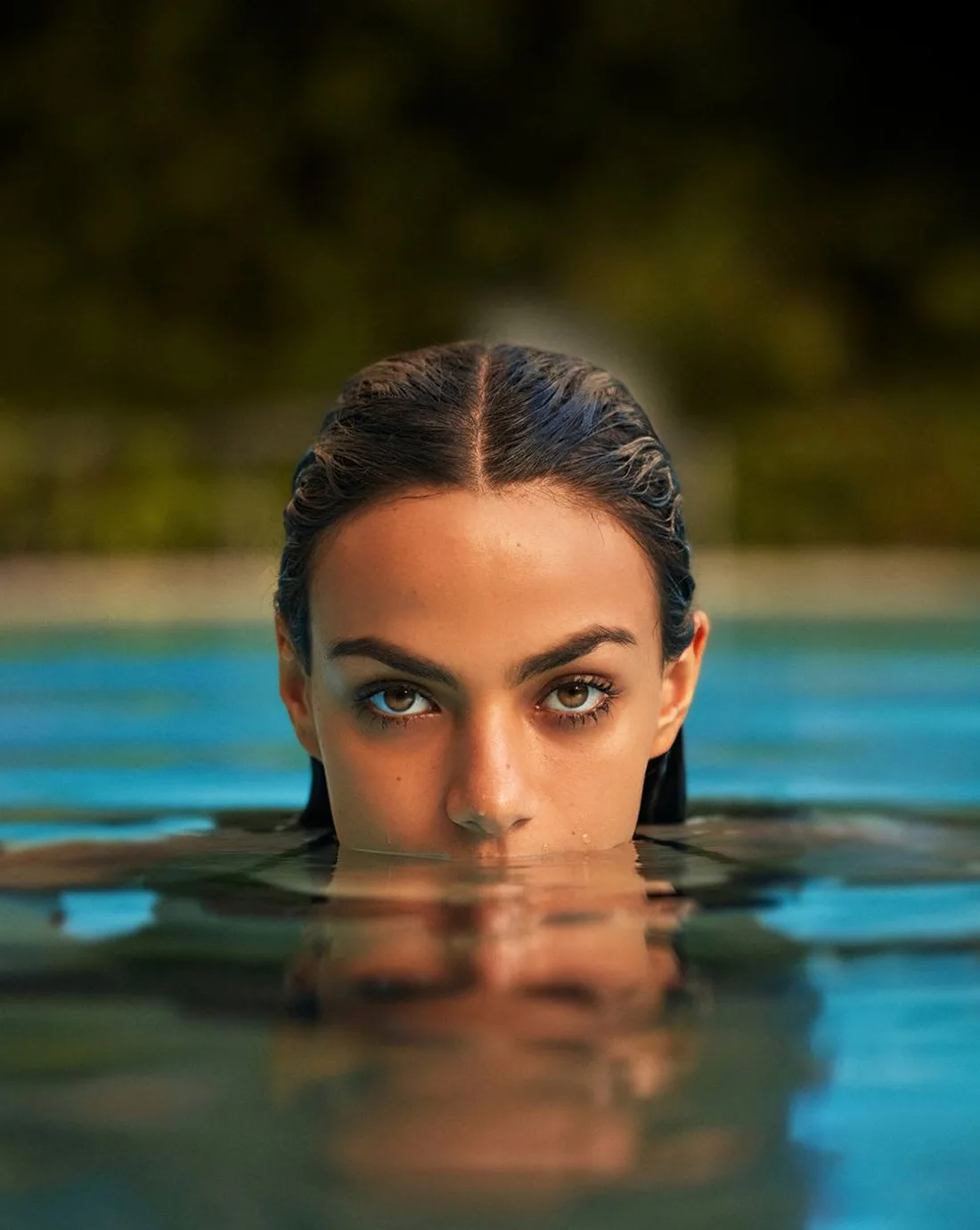 Woman with defined eyebrows emerging from pool water, testing waterproof hold